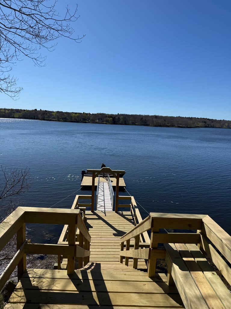 Wooden dock extending into a calm blue lake with forested shoreline and bare tree branches visible