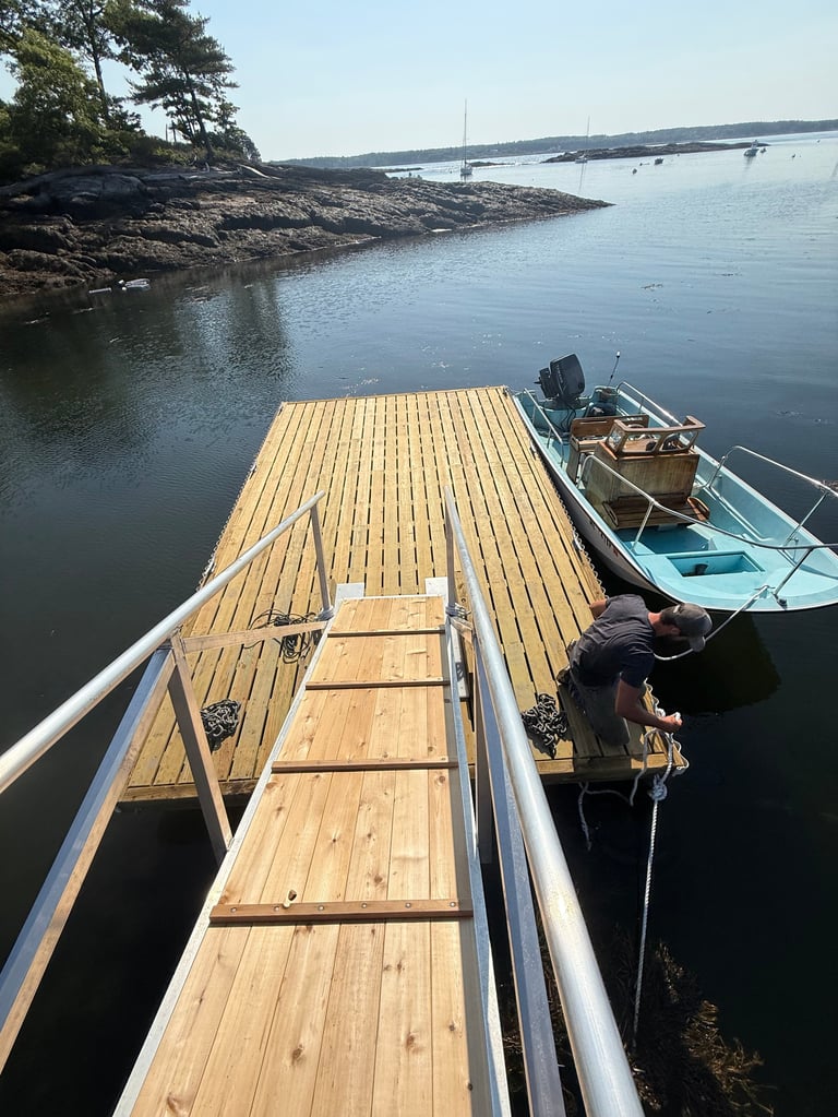 Wooden dock extending into calm waters with a blue boat moored beside it and rocky coastline in the background