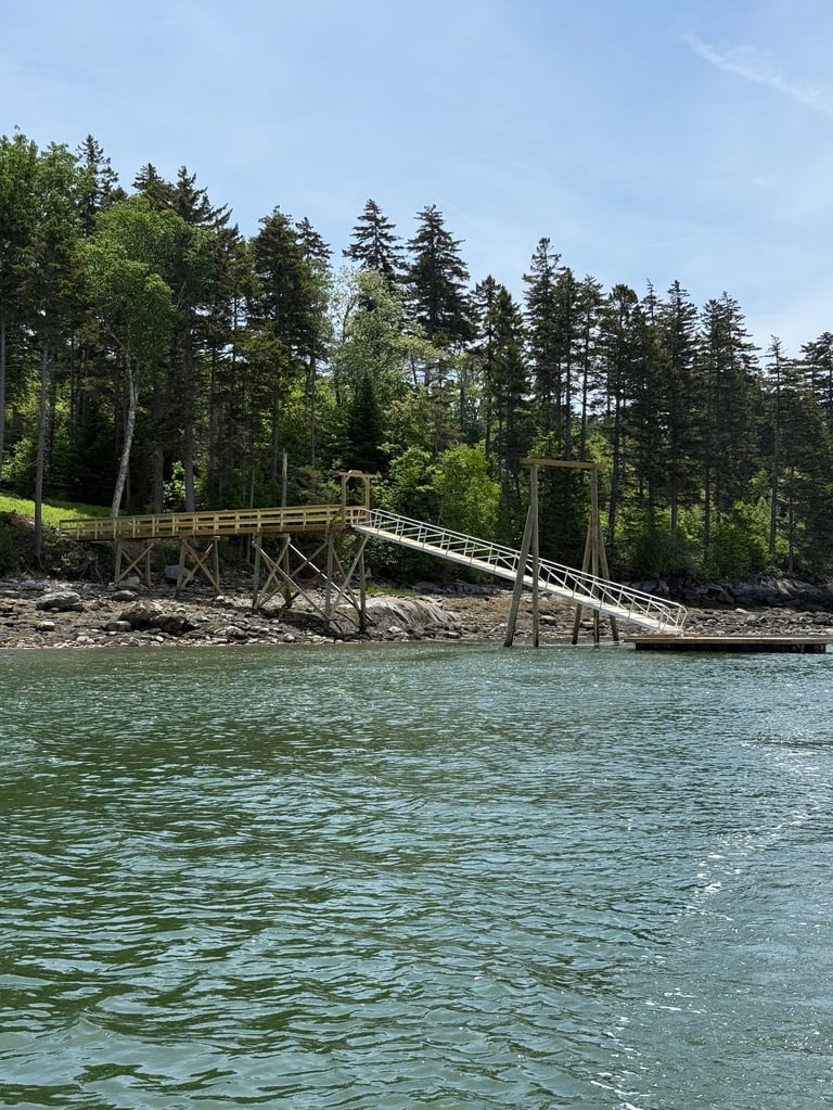 Wooden dock and boathouse on a turquoise lake surrounded by evergreen and deciduous trees under clear blue sky